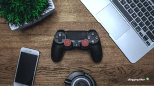 A game controller on a wooden desk beside a laptop and a phone, the featured image for How to Monetize a Gaming Blog - Blogging Titan