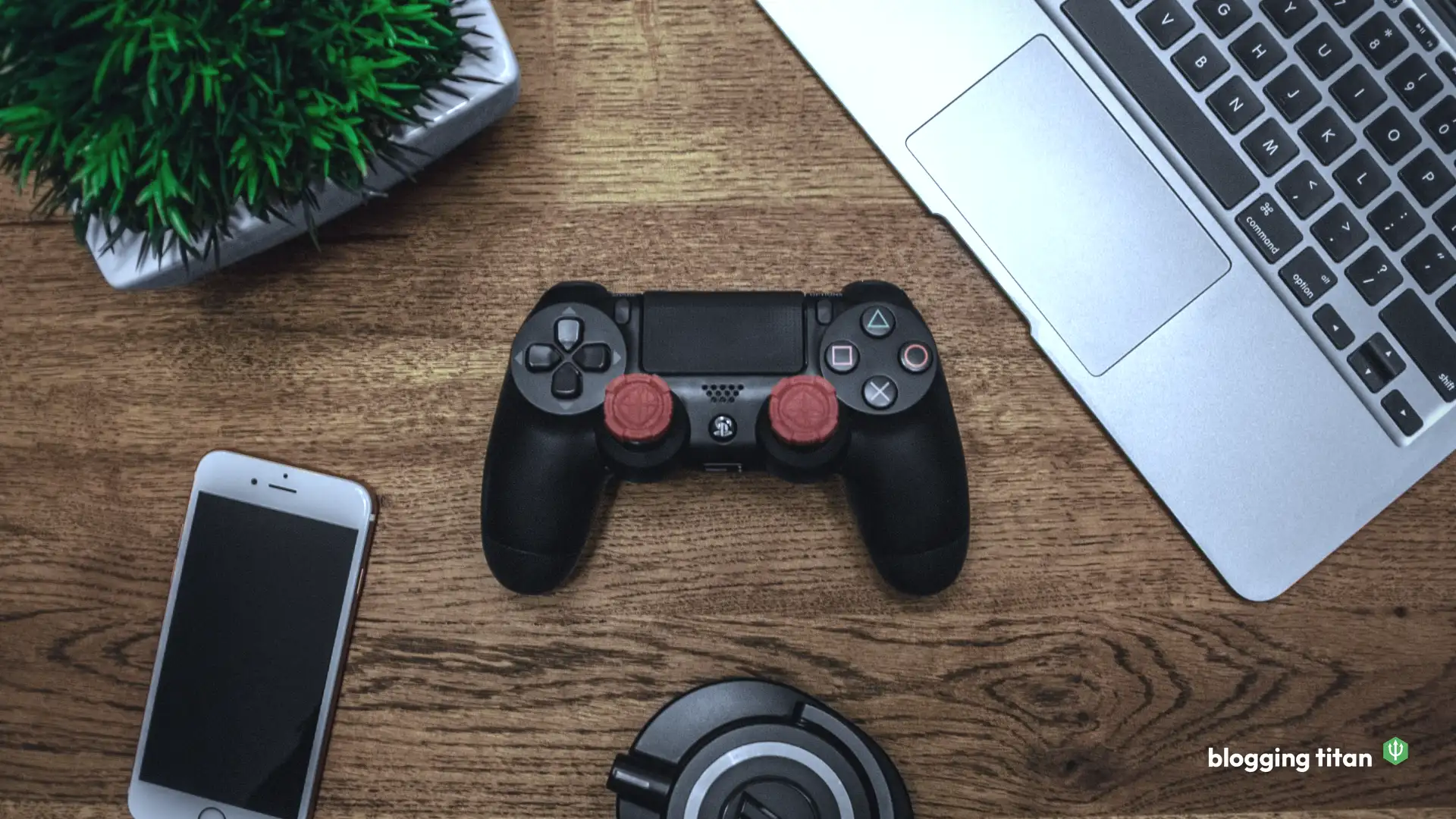 A game controller on a wooden desk beside a laptop and a phone, the featured image for How to Monetize a Gaming Blog - Blogging Titan