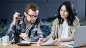 A couple going through paperwork at a kitchen table with a calculator and laptop, the featured image for How to Monetize a Personal Finance Blog - Blogging Titan